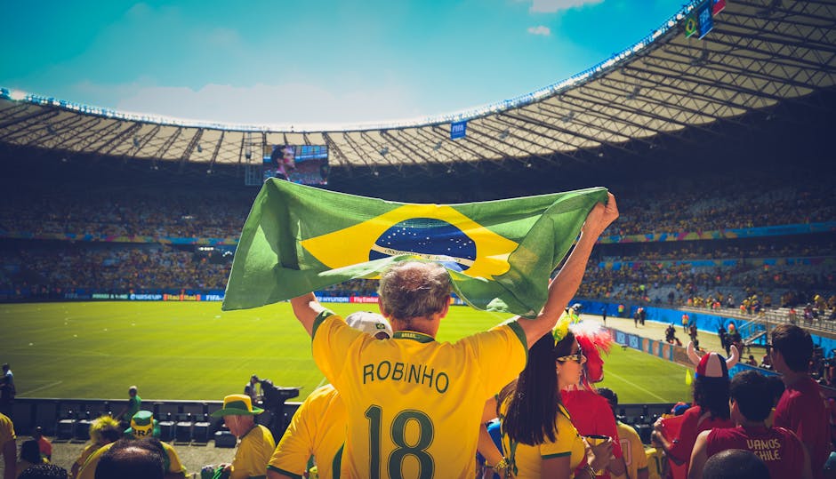 Torcedor levantando bandeira do Brasil em estádio de futebol durante a Copa do Mundo