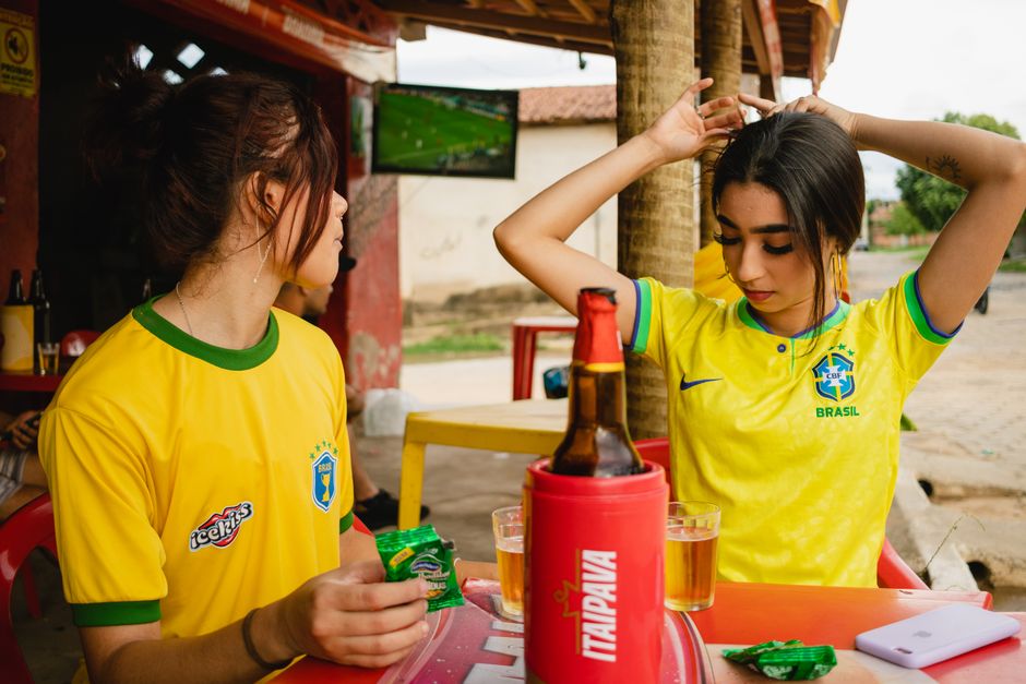 Duas mulheres em camisas da seleção brasileira torcendo em um bar durante a Copa